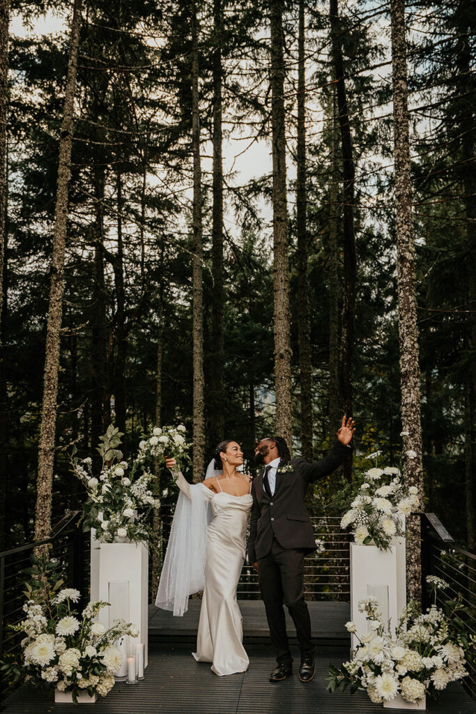 The bride and groom smiling and celebrating at Rocky Hill Weddings & Events' altar, with white flowers on either side of them.