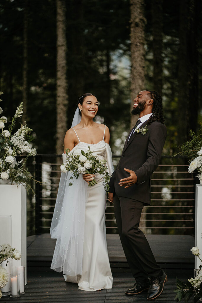 The bride and groom smiling and celebrating at Rocky Hill Weddings & Events' altar, with white flowers on either side of them.