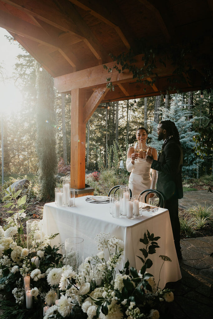 The bride and groom at the sweetheart table, toasting wine glasses. 