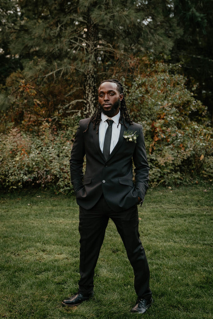 The groom posing seriously with greenery in the background. 