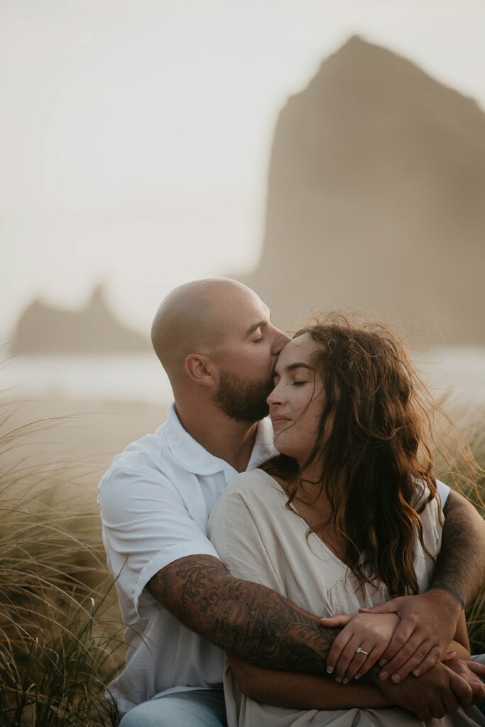 a couple sitting among beach grass and holding each other close. 