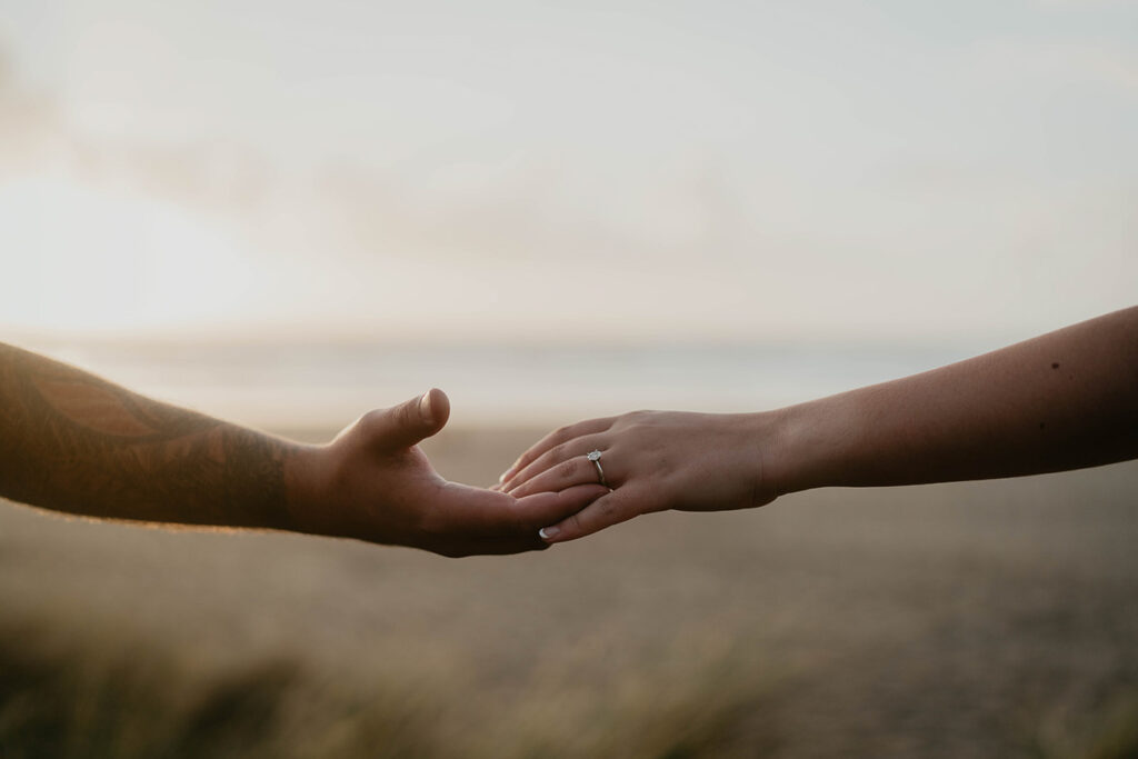 a newly engaged couple holding hands with the beach in the background. 