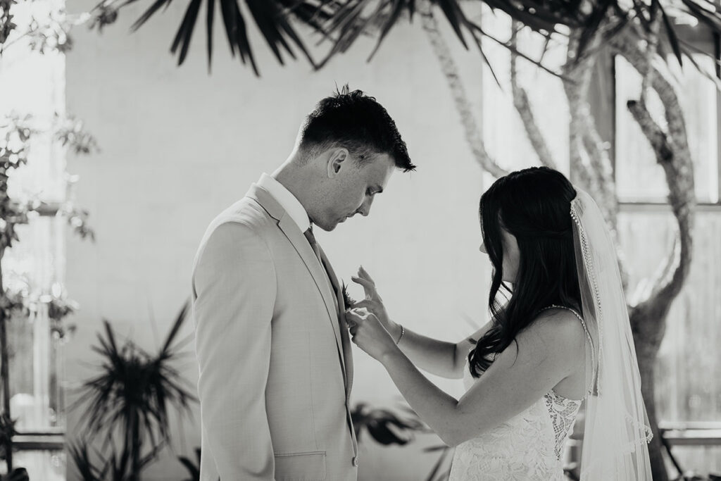 The bride pinning on a boutonniere on her husband. 