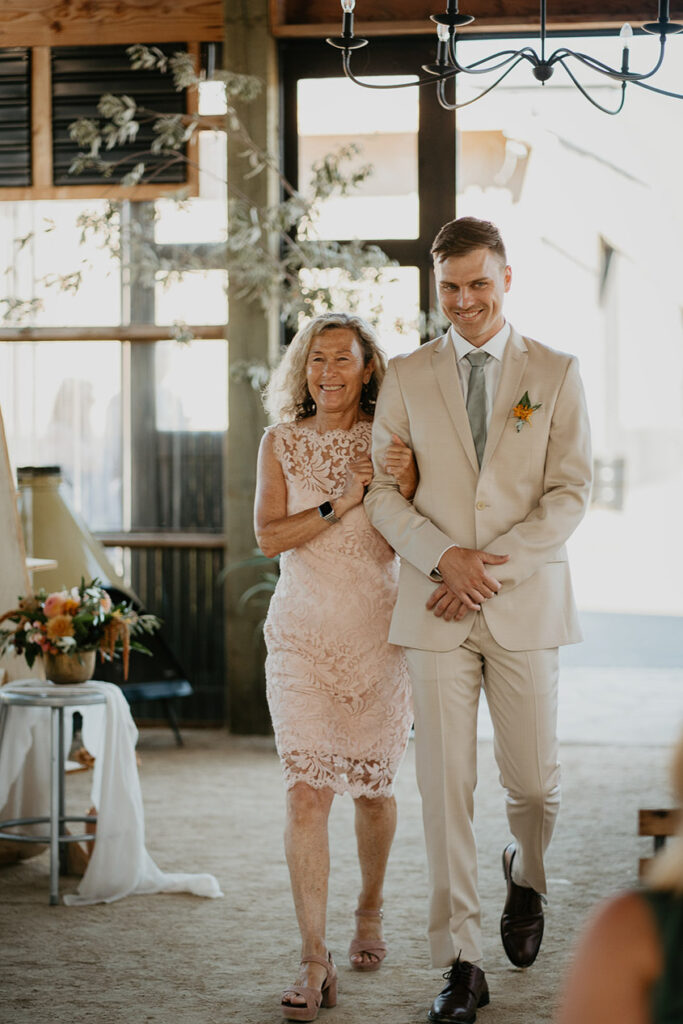 the groom walking down the isle with his mom. 