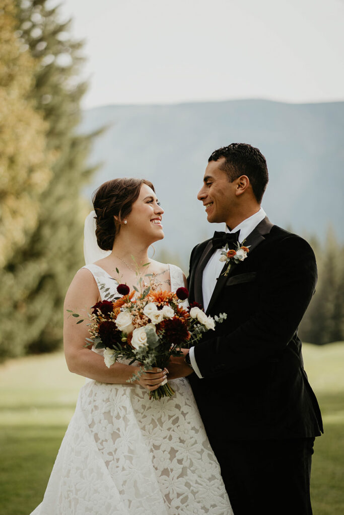 the bride and groom smiling at each other and holing flowers. 