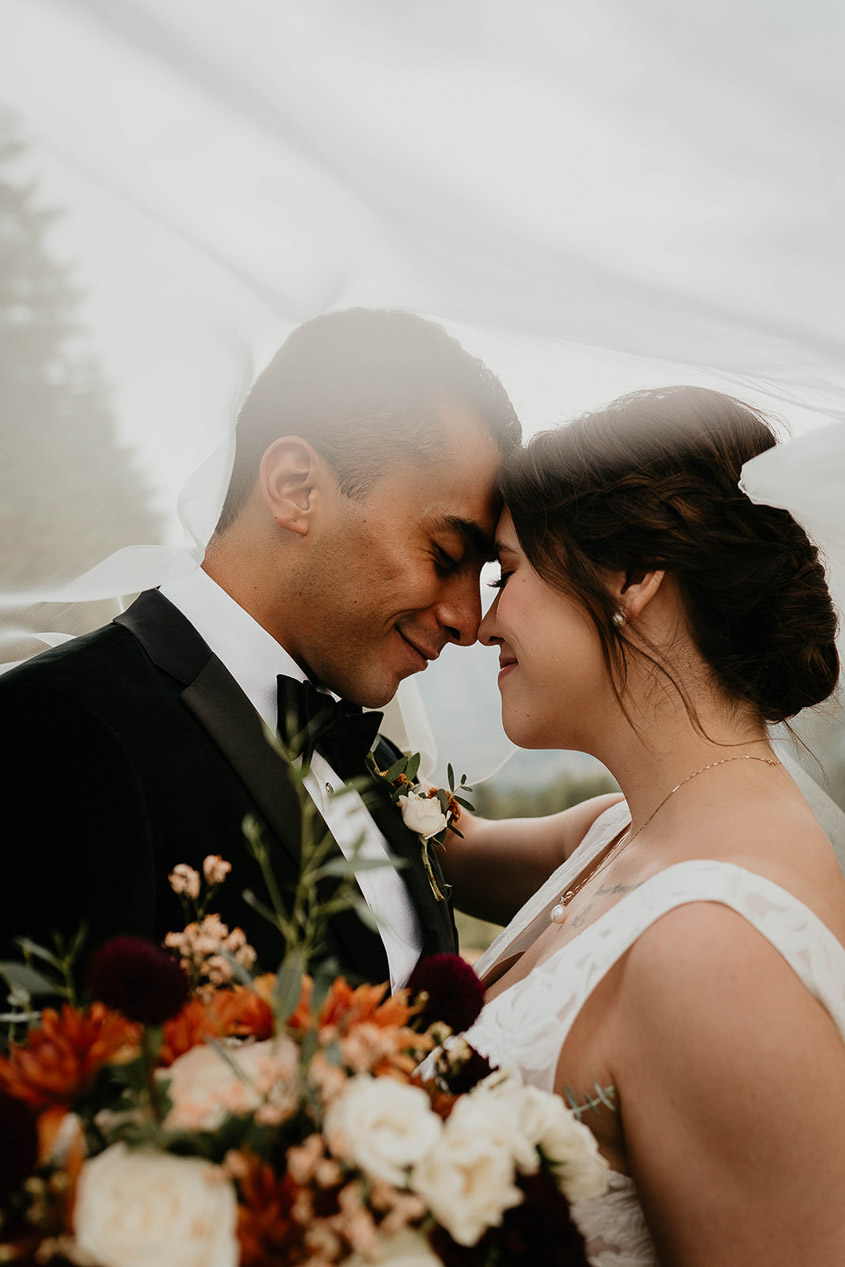 the bride and groom holding each other close with the vail around them. 