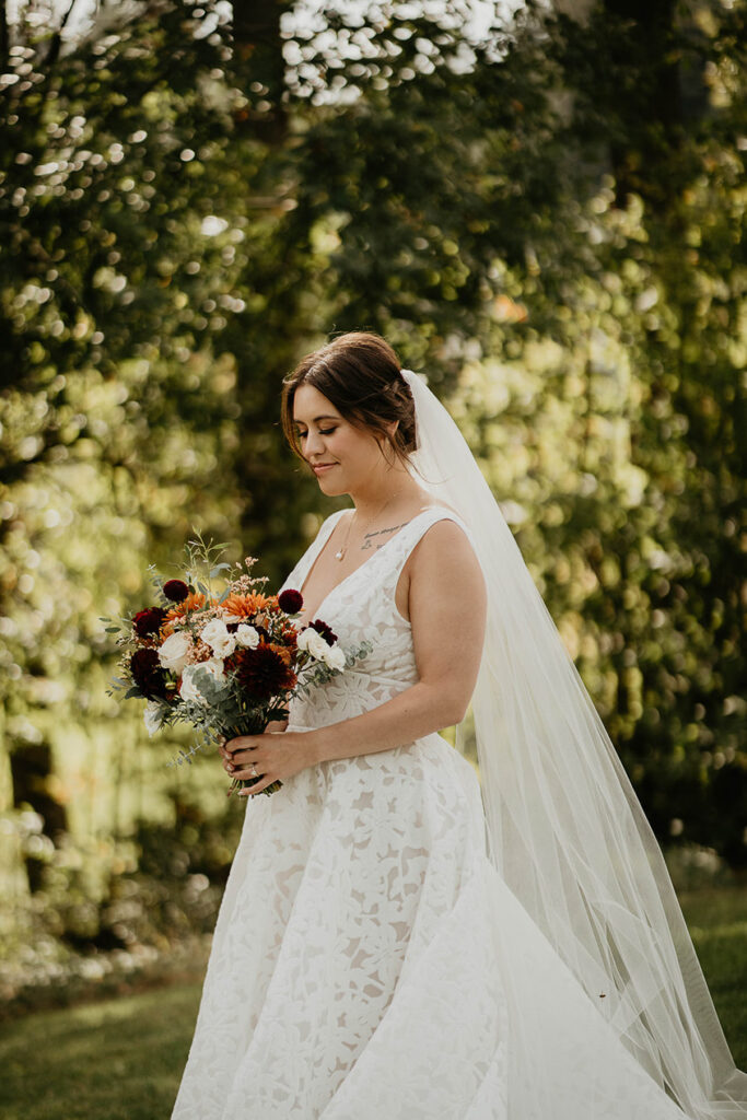 the bride in a moment of thought with greenery and trees in the background. 