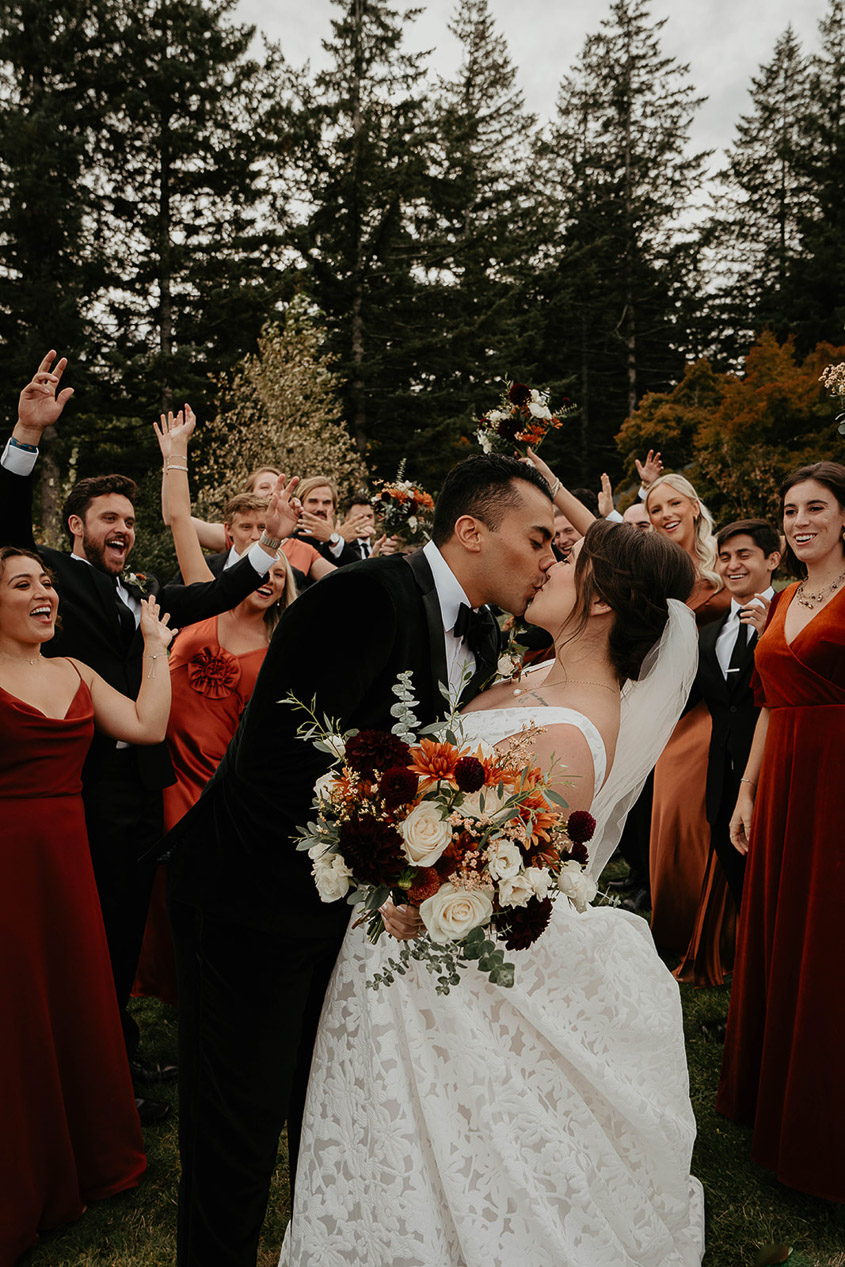 the bride and groom kissing, surrounded by their wedding party. 