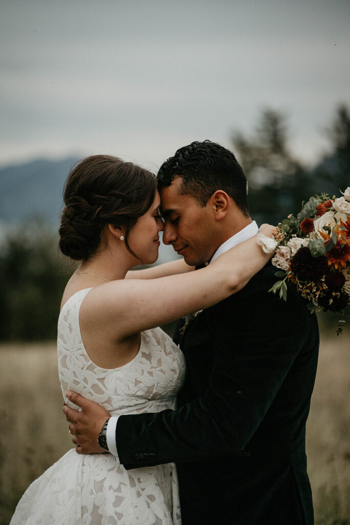 the newlyweds hugging with a field and pine trees in the background. 