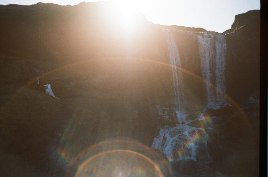 Bride and groom hold hands while walking in front of a waterfall in Iceland