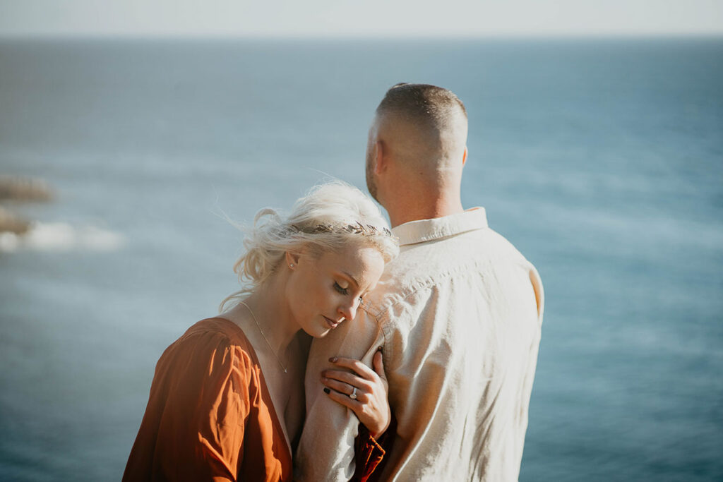 The wife holding her husband with the Pacific Ocean in the background. 