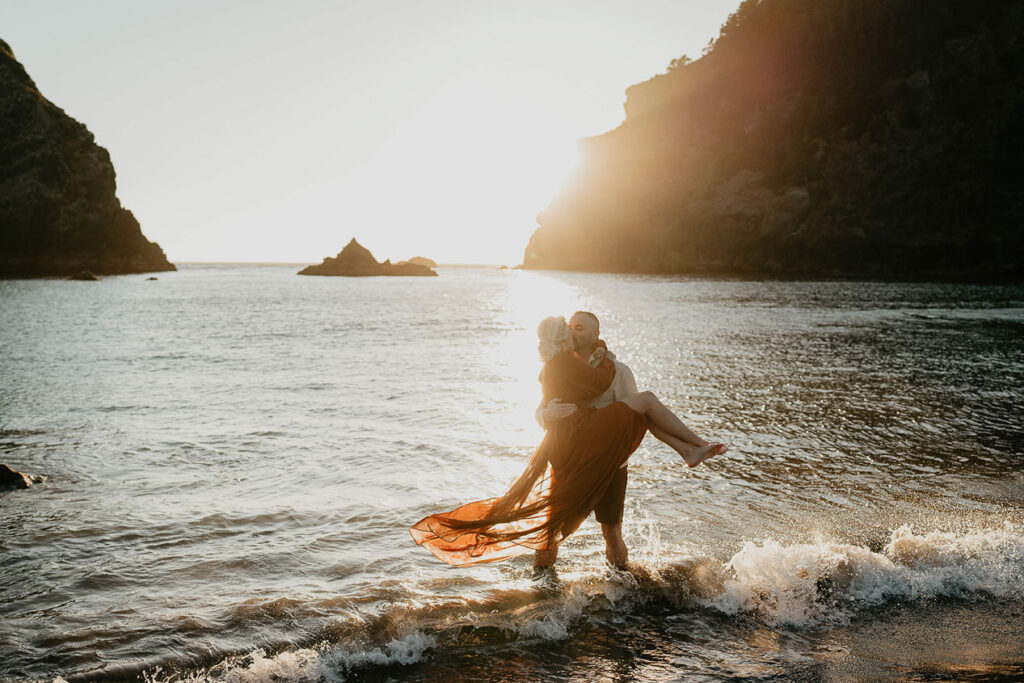 The husband holding his wife as a wave crashes into them. 