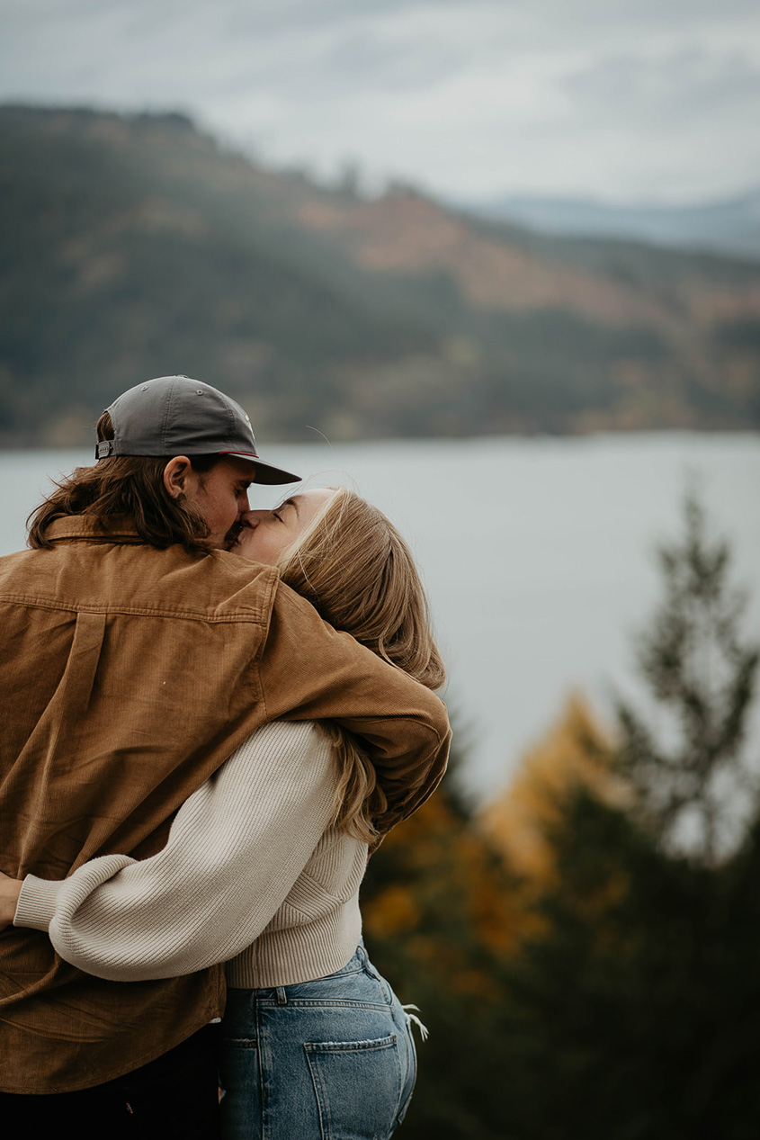 A newly engaged couple kissing with the Columbia river in the background. 