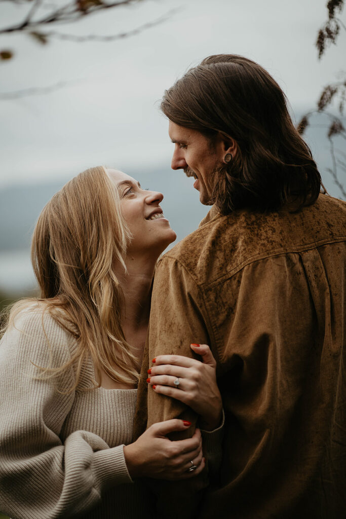 a newly engaged couple holding each other under a tree. 