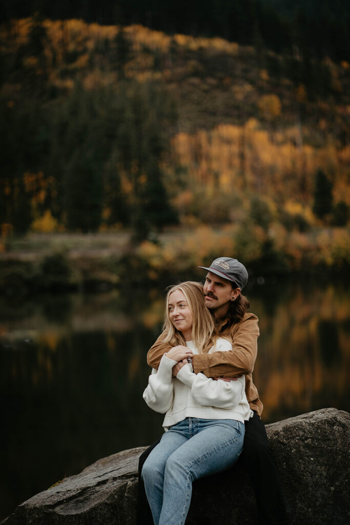 A newly engaged couple holding each other with the Columbia river and evergreen trees in the background. 