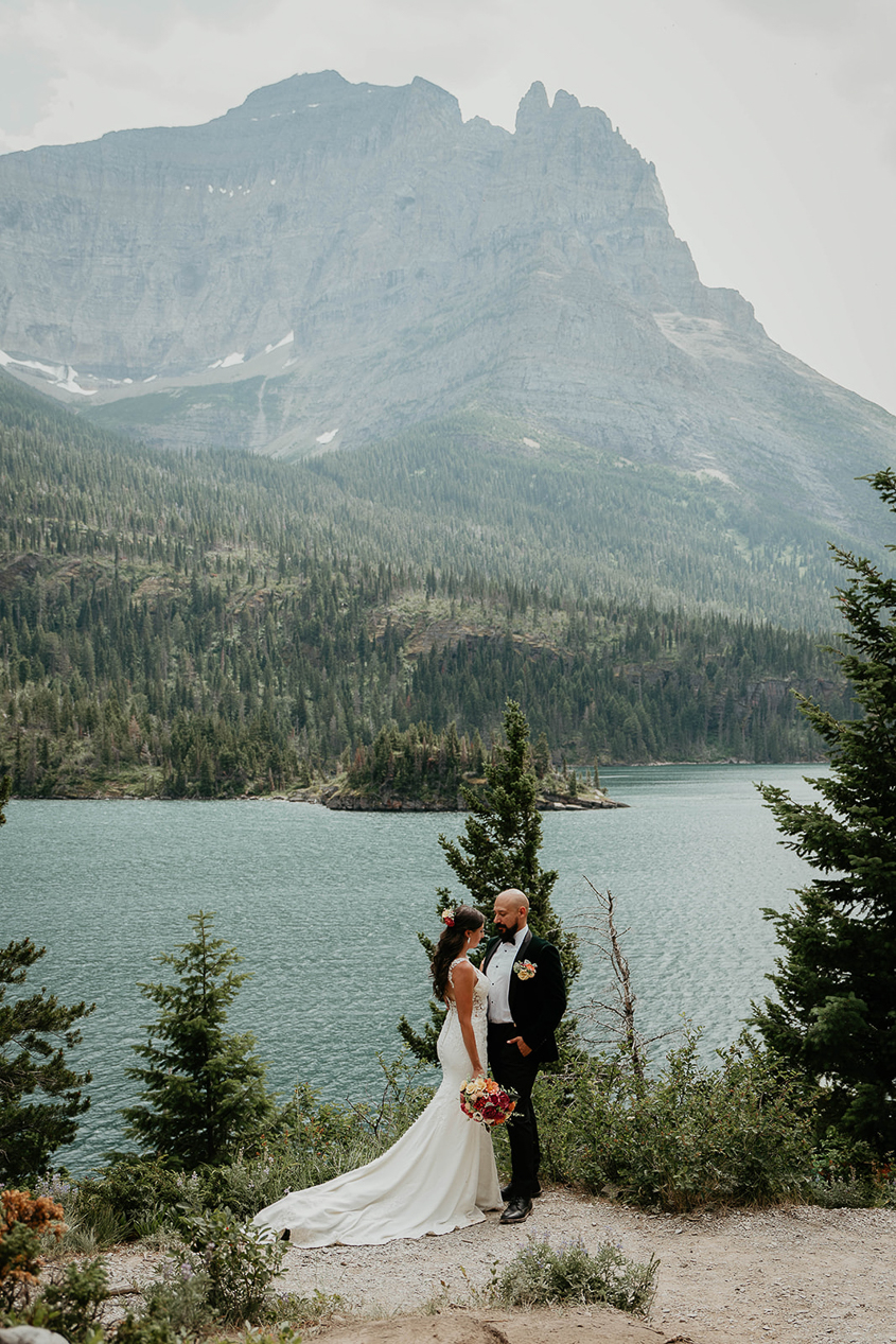 The newlyweds standing close with a lake and mountain in the background. 