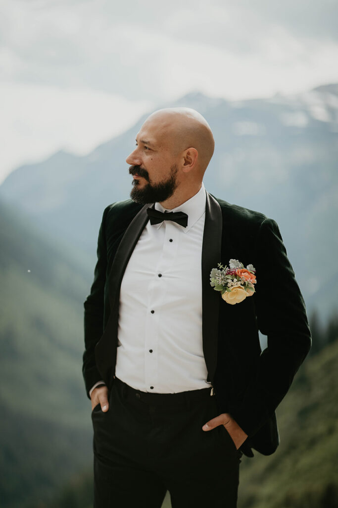 The groom posing and looking off into the distance with large mountains around him. 