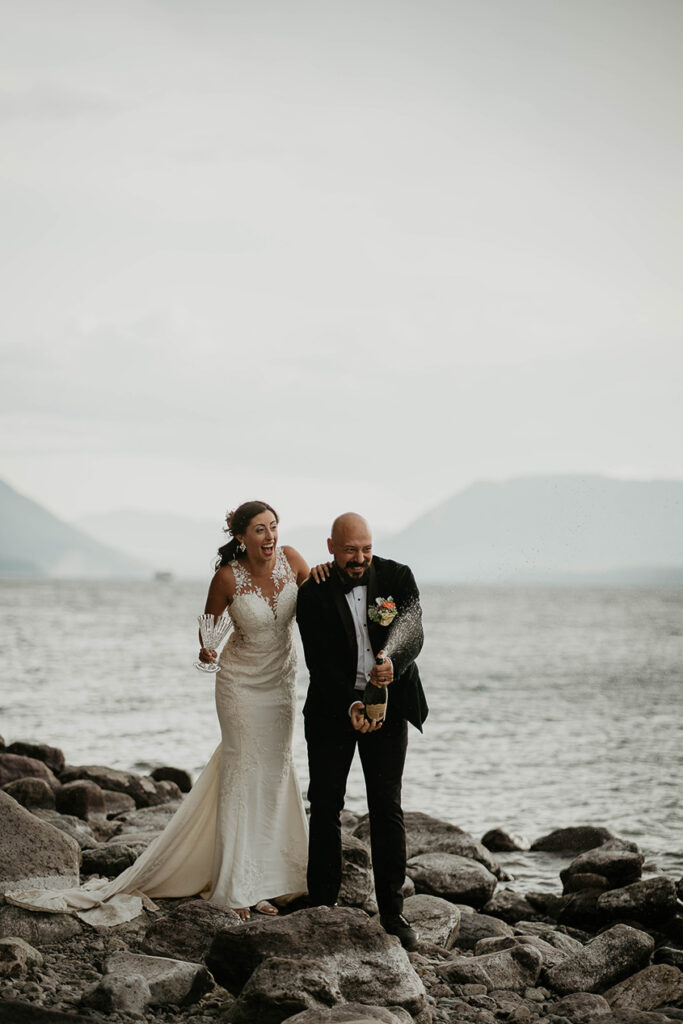 The couple popping a bottle of champagne on the shores of a lake in Glacier National Park. 