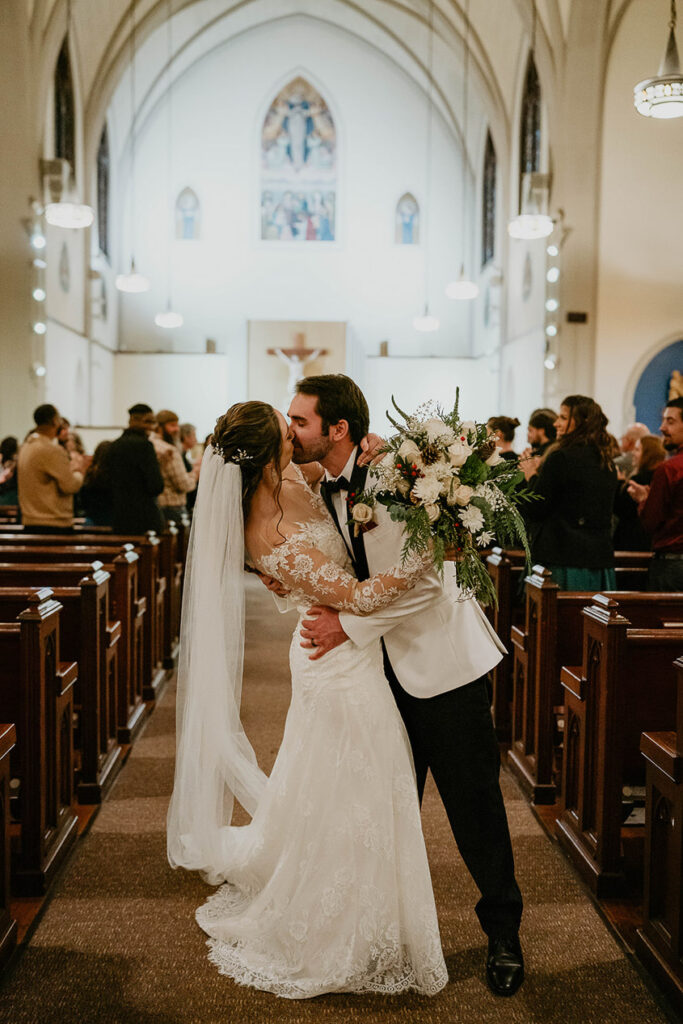 a newlywed couple kissing as they walk down the isle. 