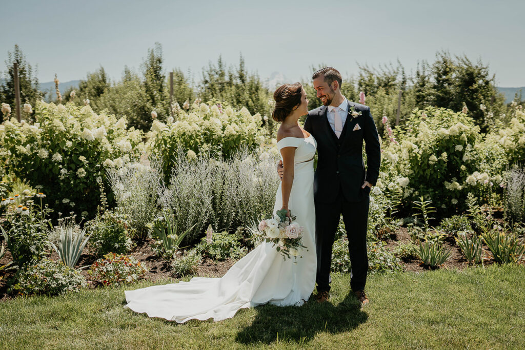 The bride and groom smiling at each other with flowers in the background. 