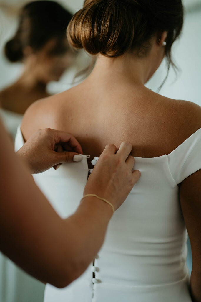 a bridesmaid helping button up the bride's wedding dress. 