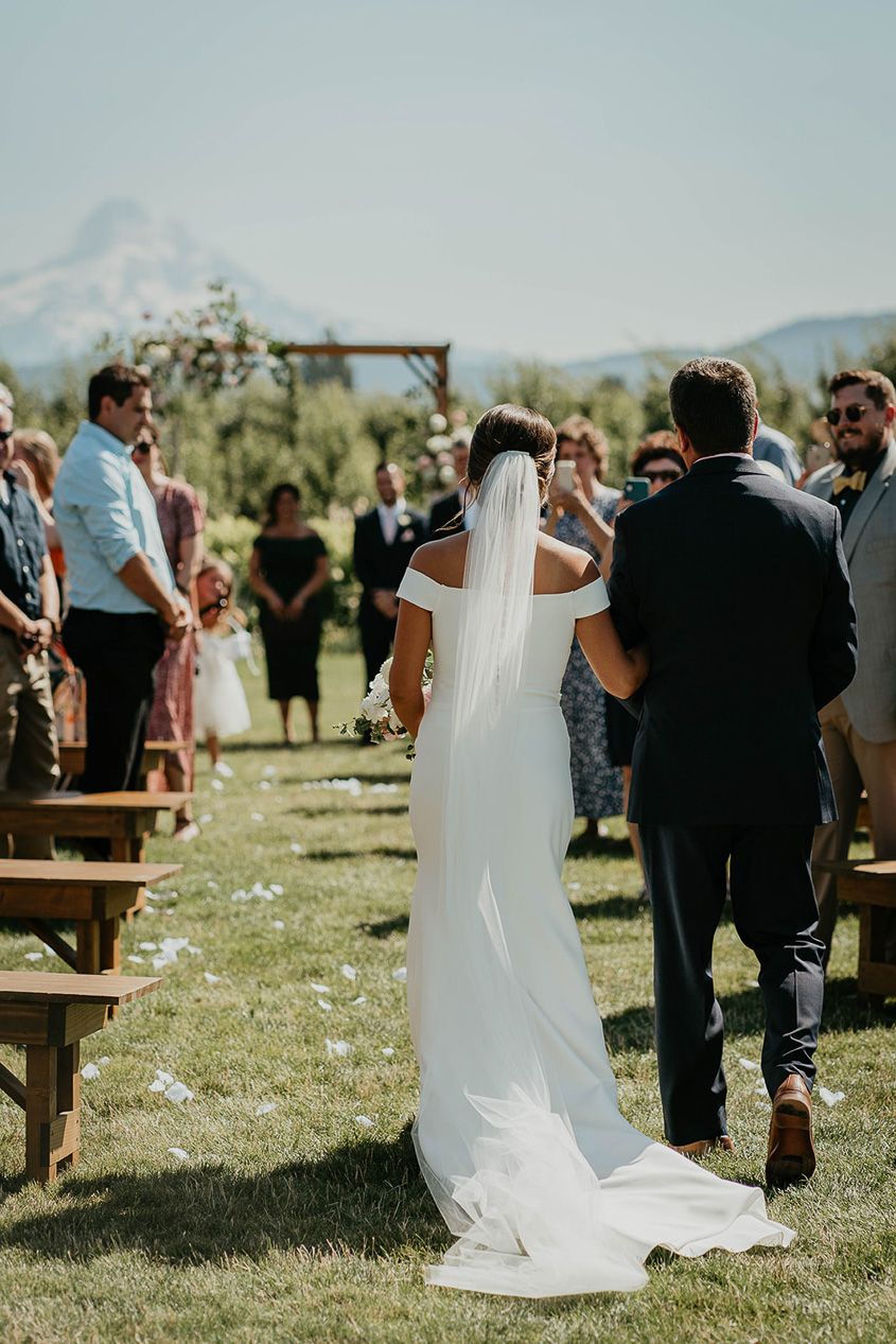 The bride and her father walking down the isle at The Orchard Hood River with Mt. Hood in the background. 