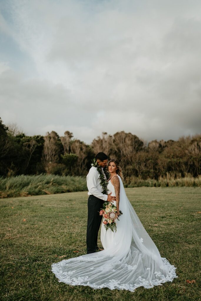 Bride and groom stand in a lawn taking wedding photos during their elopement in Hawaii