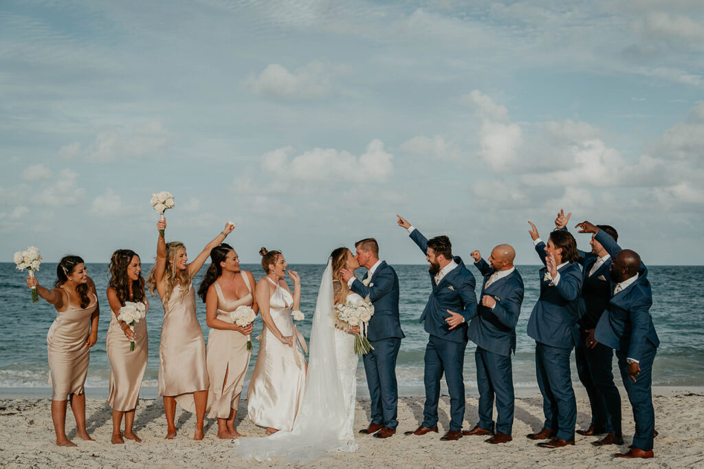 The bride and groom kissing surrounded by their wedding party. 