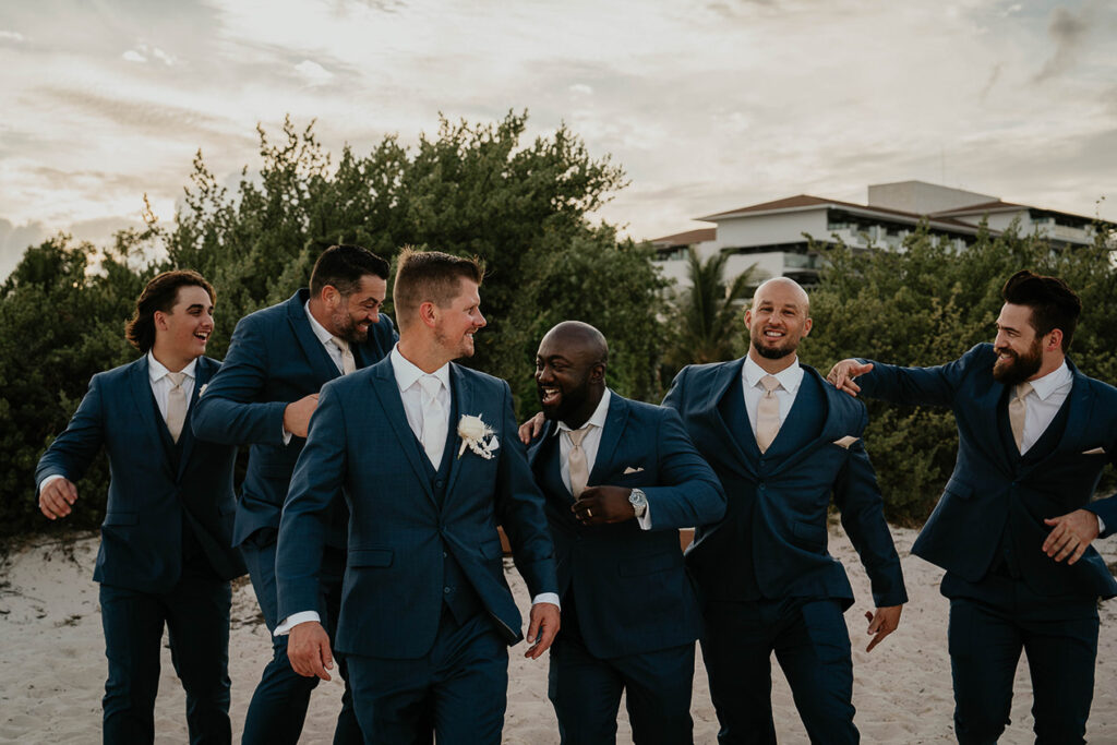 the groomsman and groom laughing and playing around on the beach. 