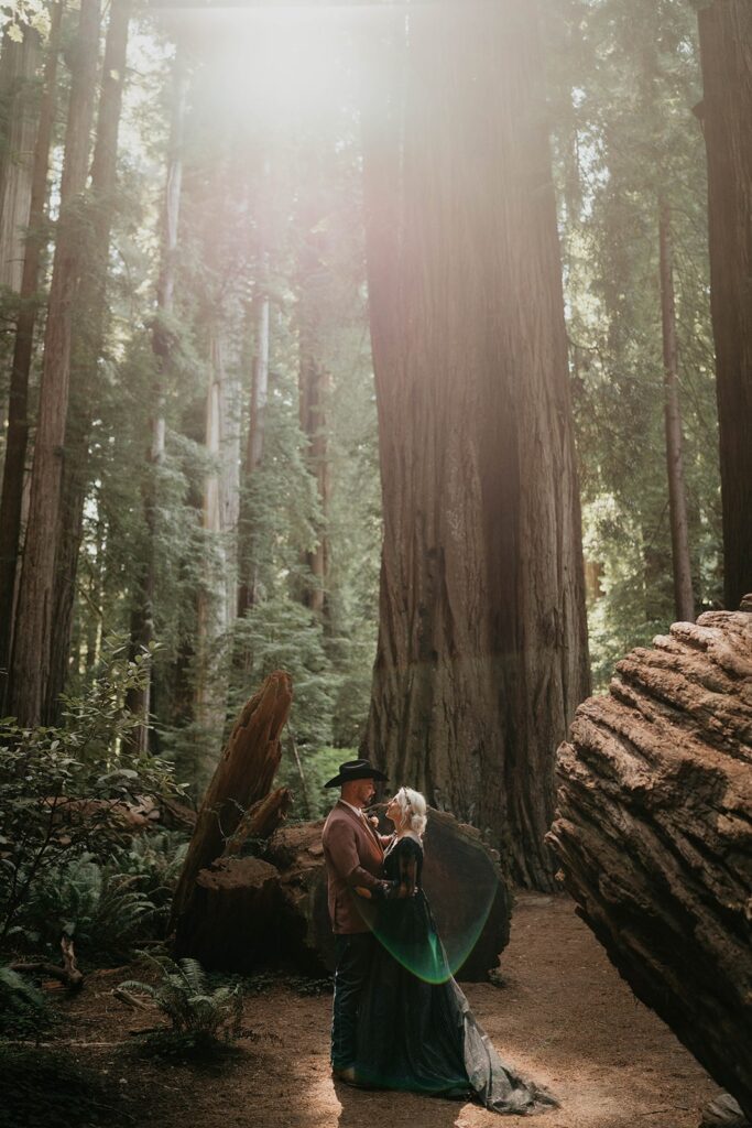 Bride and groom kiss in front of a redwood tree during their forest elopement on the Oregon Coast