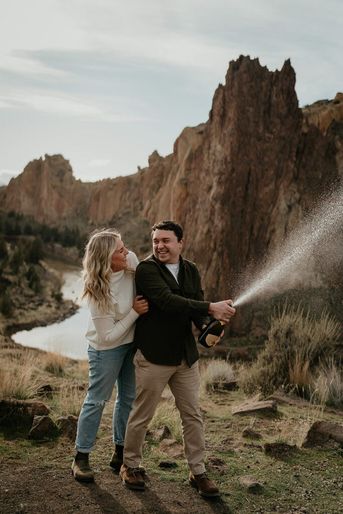 A newly engaged couple spraying a bottle of champagne at Smith Rock.