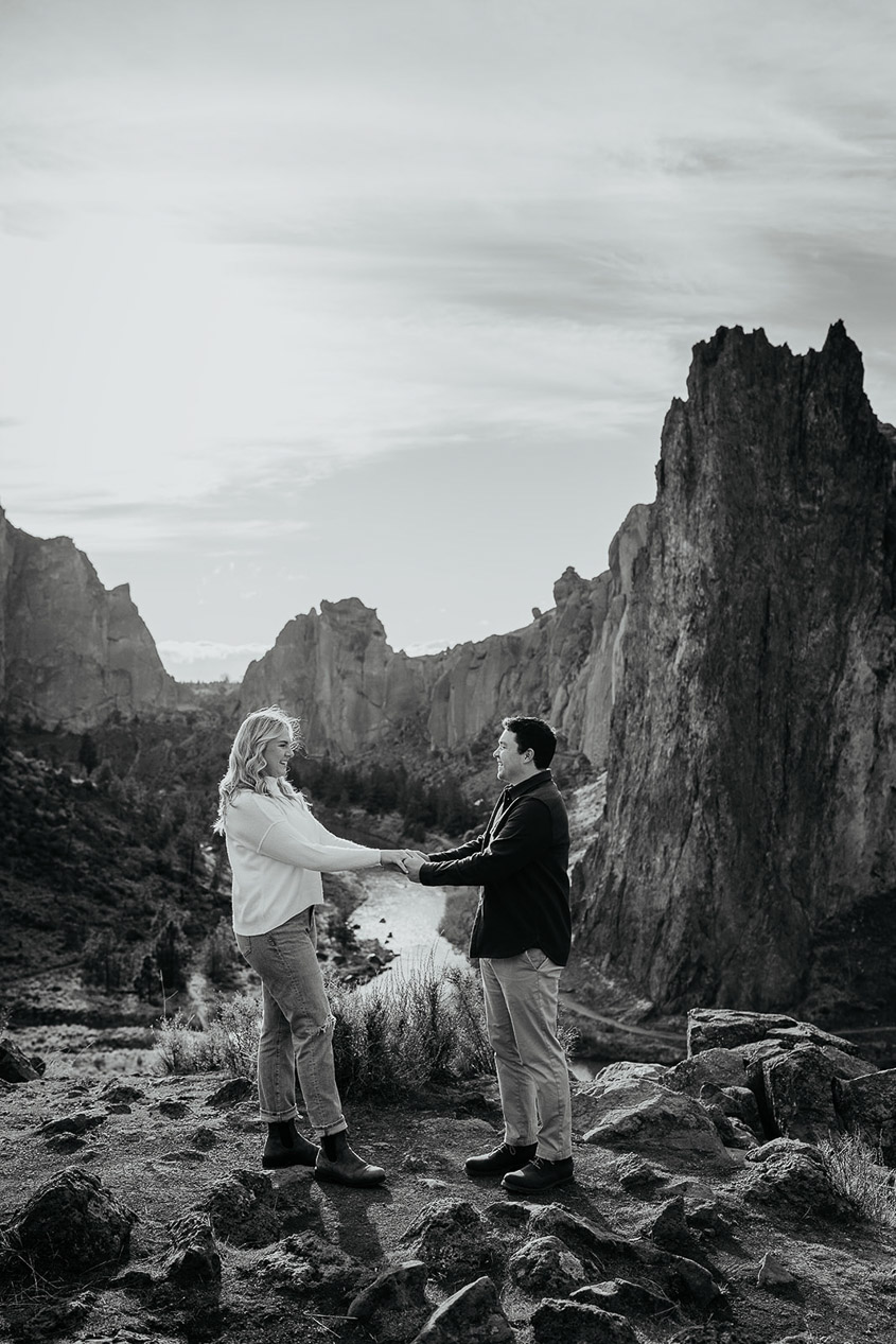 The couple holding hand with a river and rocks in the background at their Smith Rock engagement session.