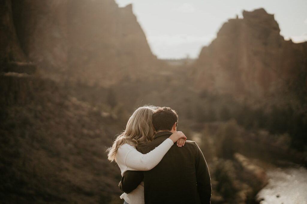 A couple embracing each other with big rocks in the background. 