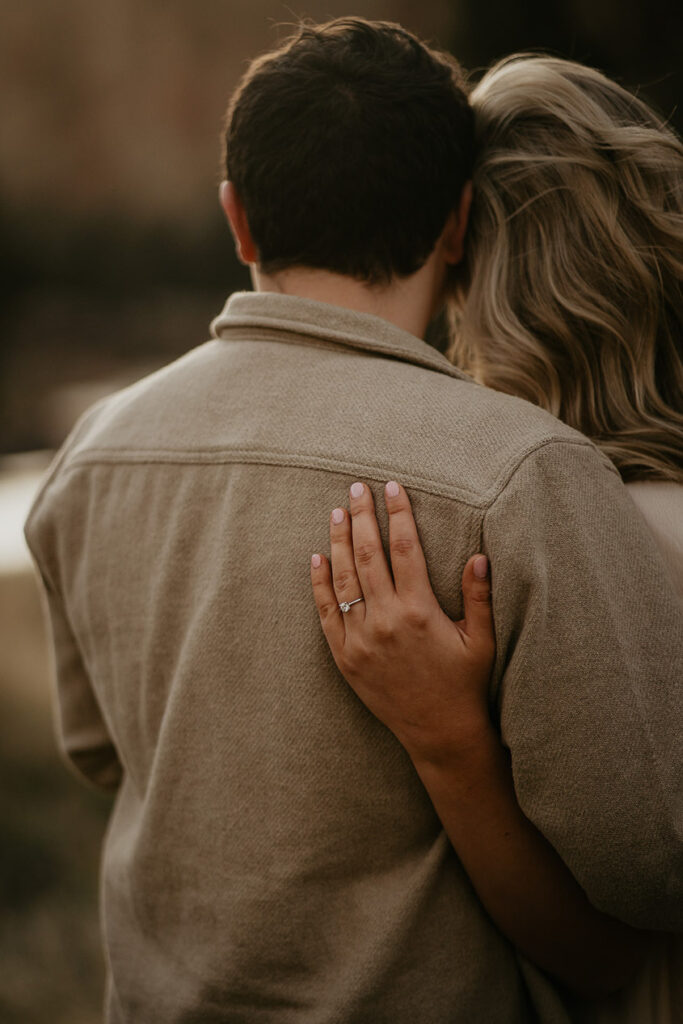 a couple holding each other, showing off the engagement ring. 