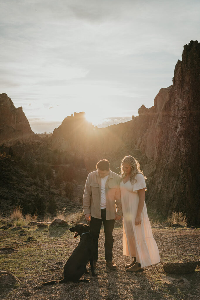 a couple holding hands and looking lovingly at their dog during their Smith Rock engagement session. 