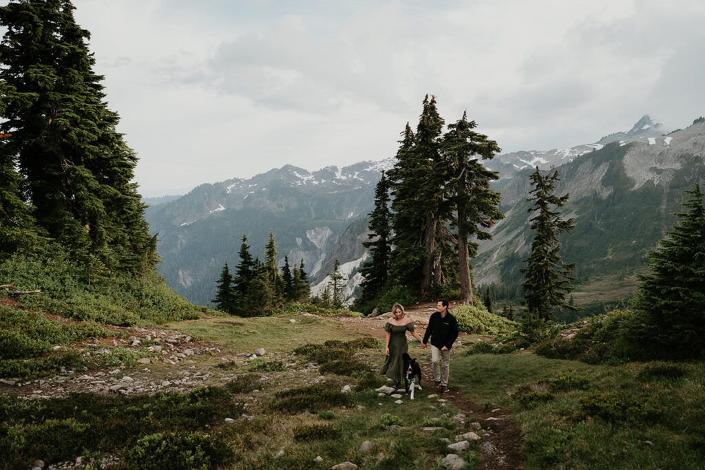 A couple walking with their dog in the mountains.