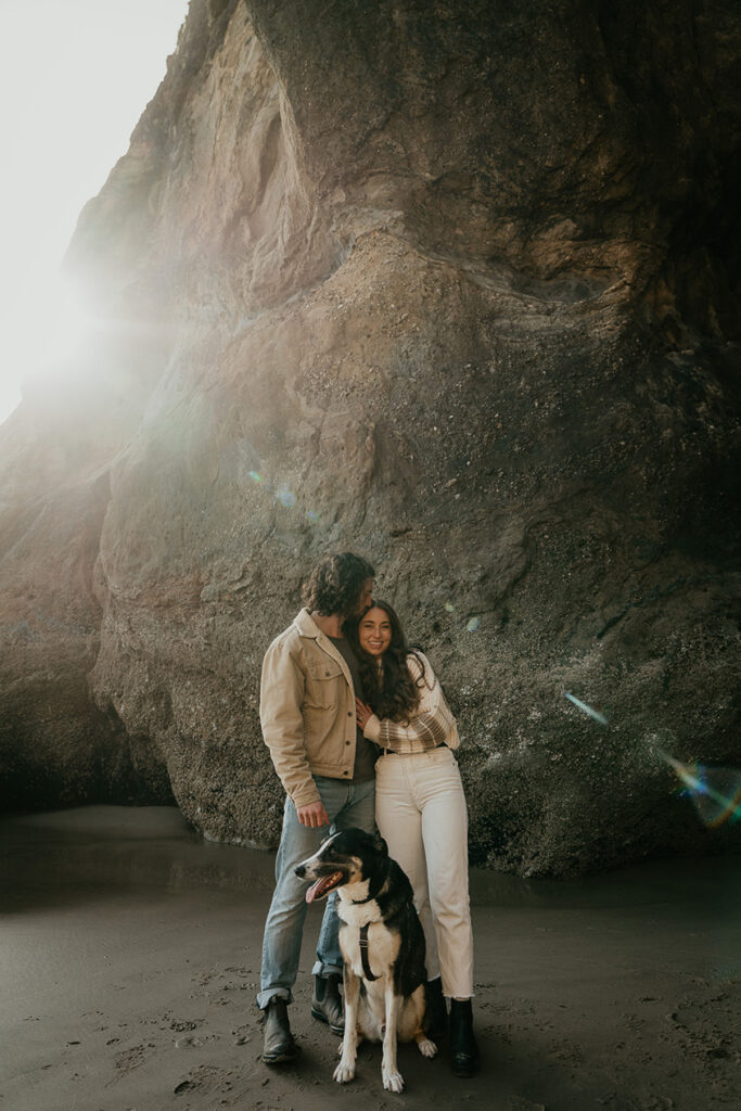 A couple posing with their dog on the beach. 