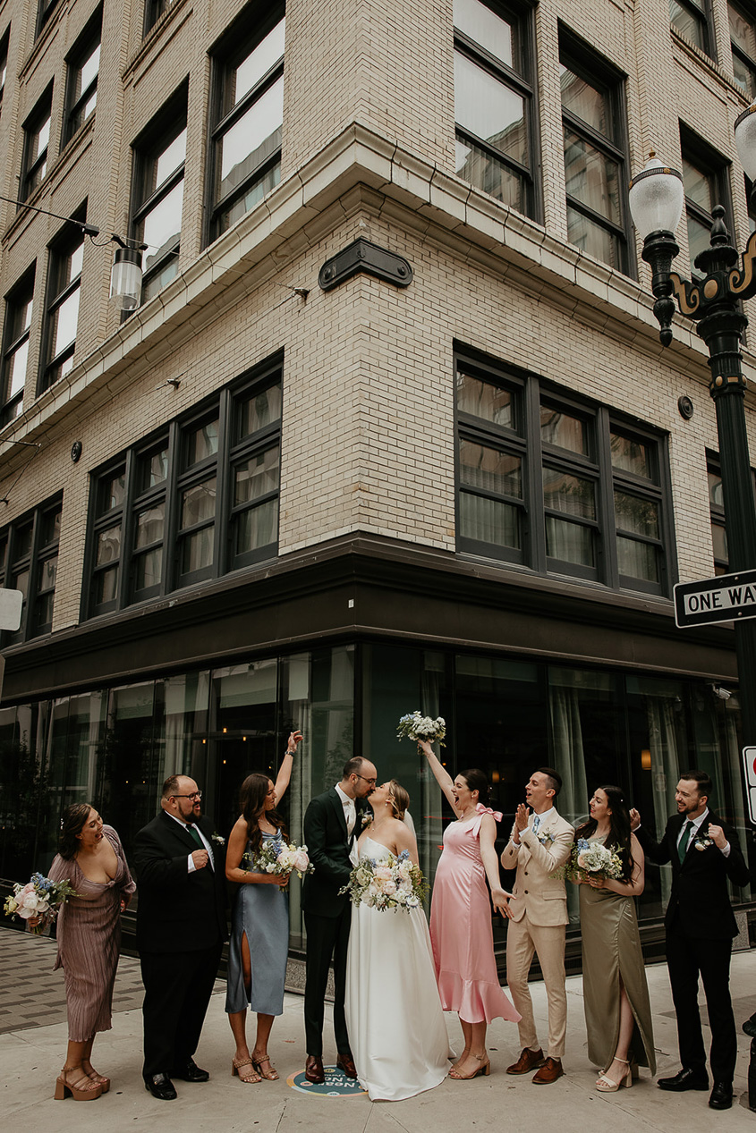 the bride and groom kissing with their wedding party next to them. 