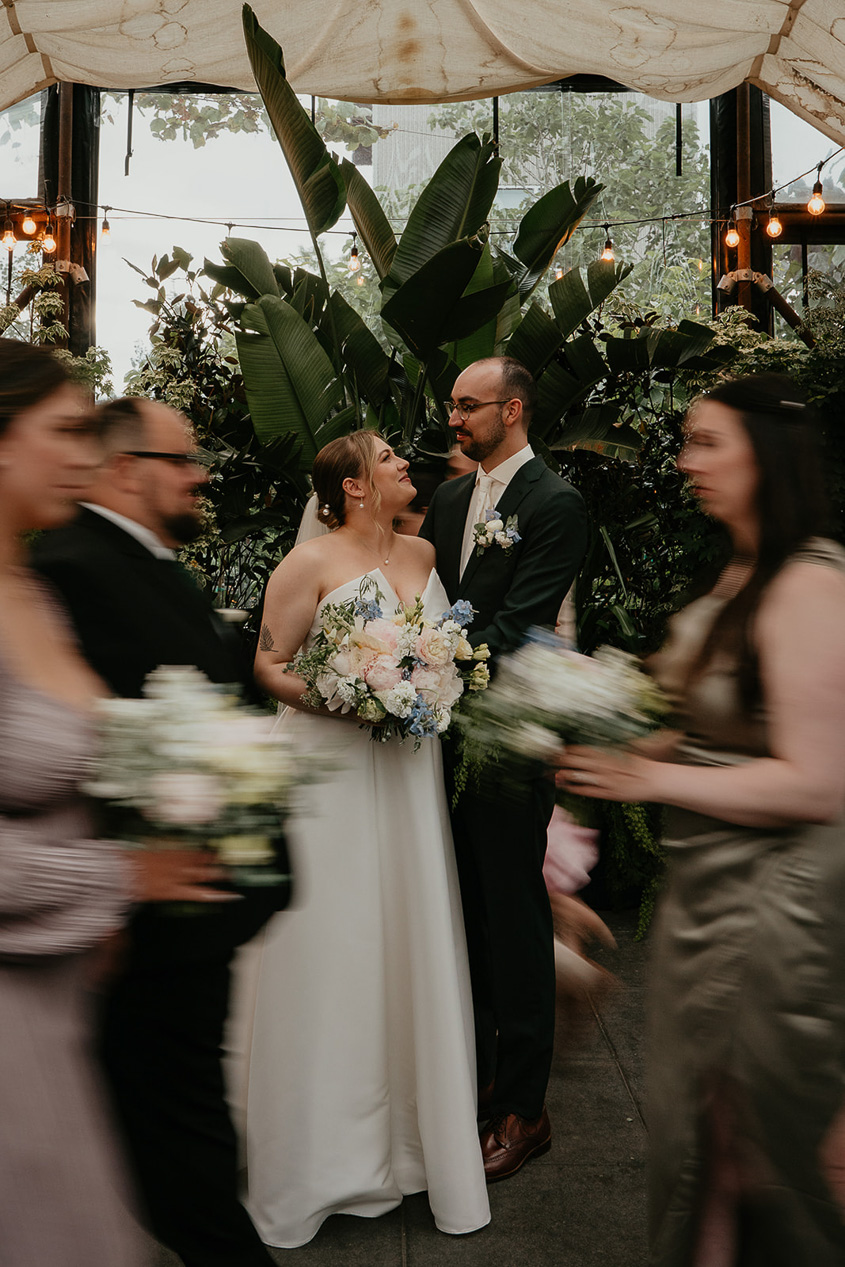 The newlyweds looking deeply at each other while their wedding party walks by.