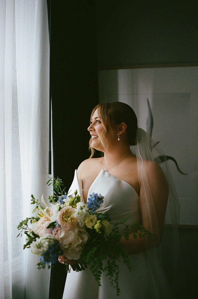 the bride looking out a window with her bouquet. 