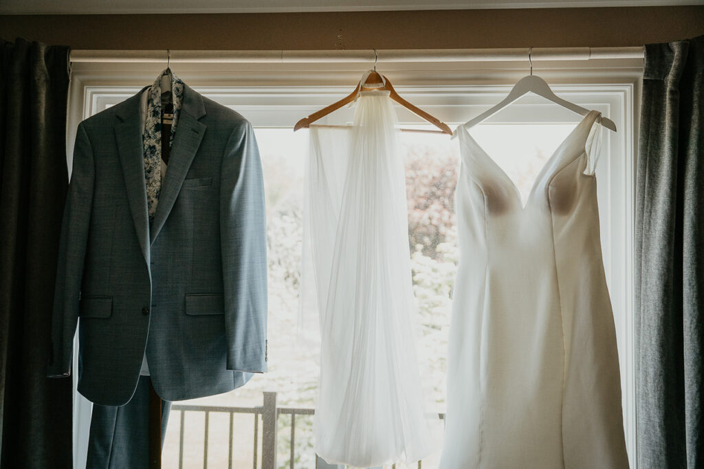 the groom's jacket, and the bride's wedding dress and veil hanging in front of a window. 