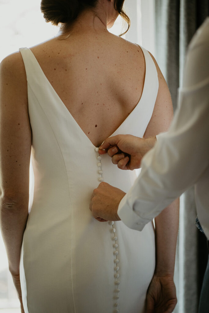 the groom zipping up the bride's dress. 