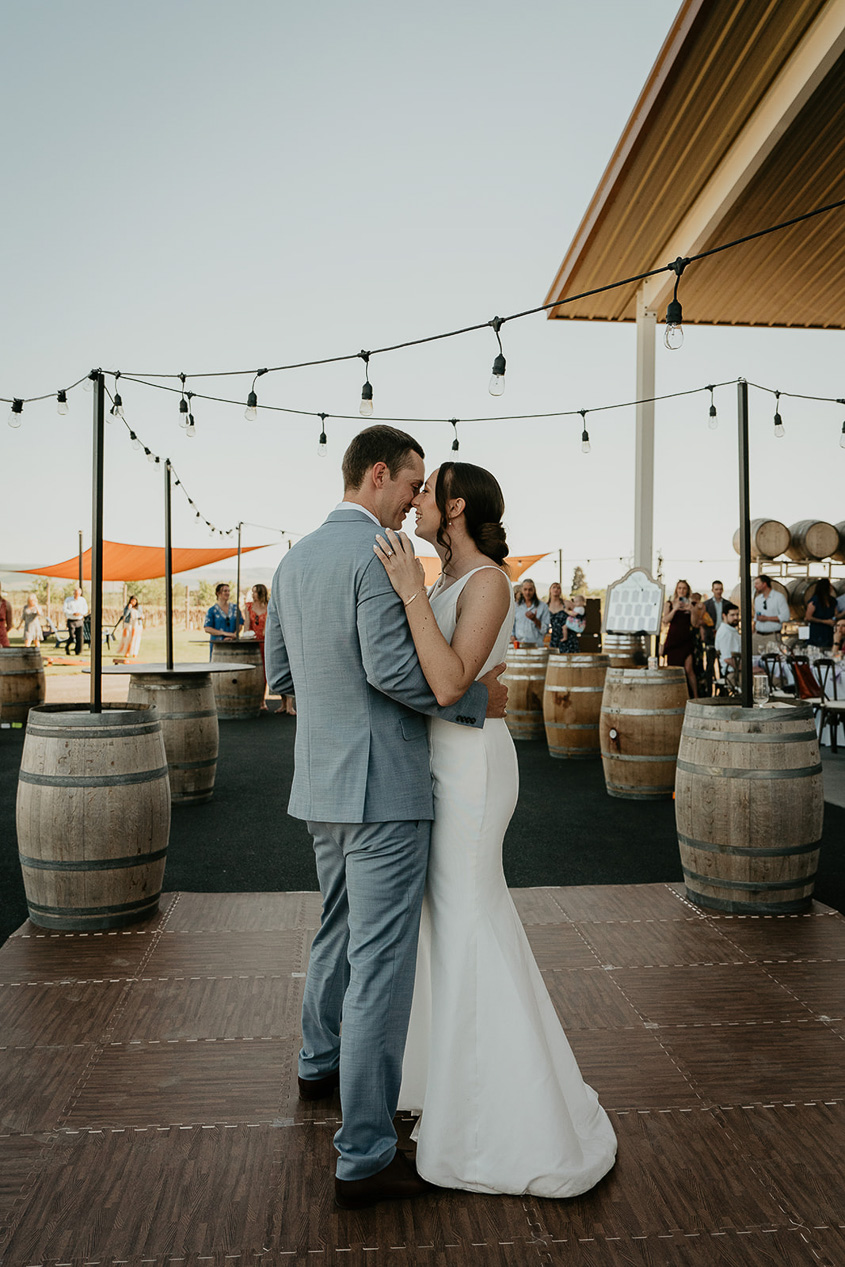 the newlyweds dancing with wine barrels and bistro lighting around them. 