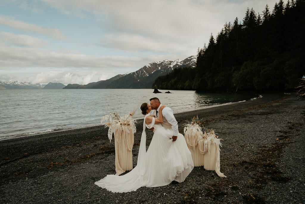 A couple kissing on the beach with the ocean and mountains in the background while they elope in Alaska. 