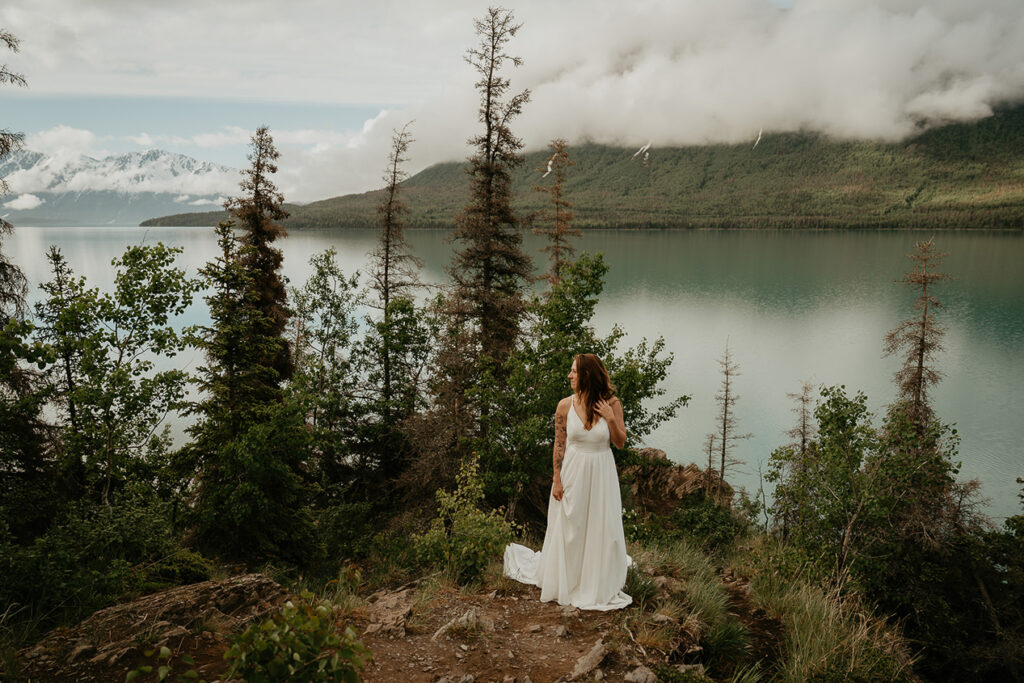 The bride standing on the cliffside with the ocean and mountains in the background. 