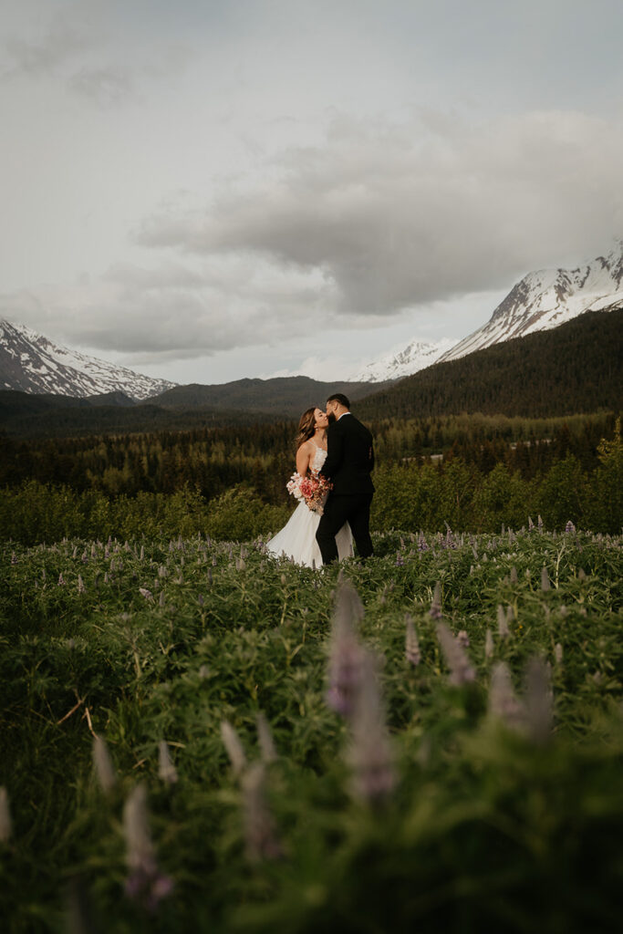 A couple kissing in a field with mountains in the background. 