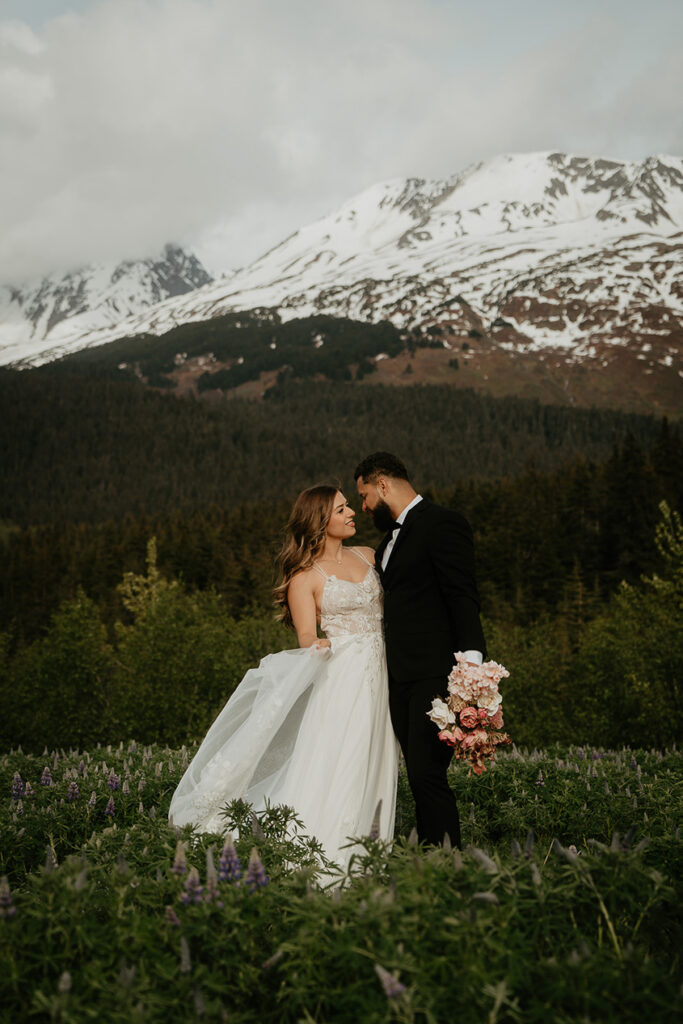 A couple hugging each other in a field with mountains in the background while they elope in Alaska. 