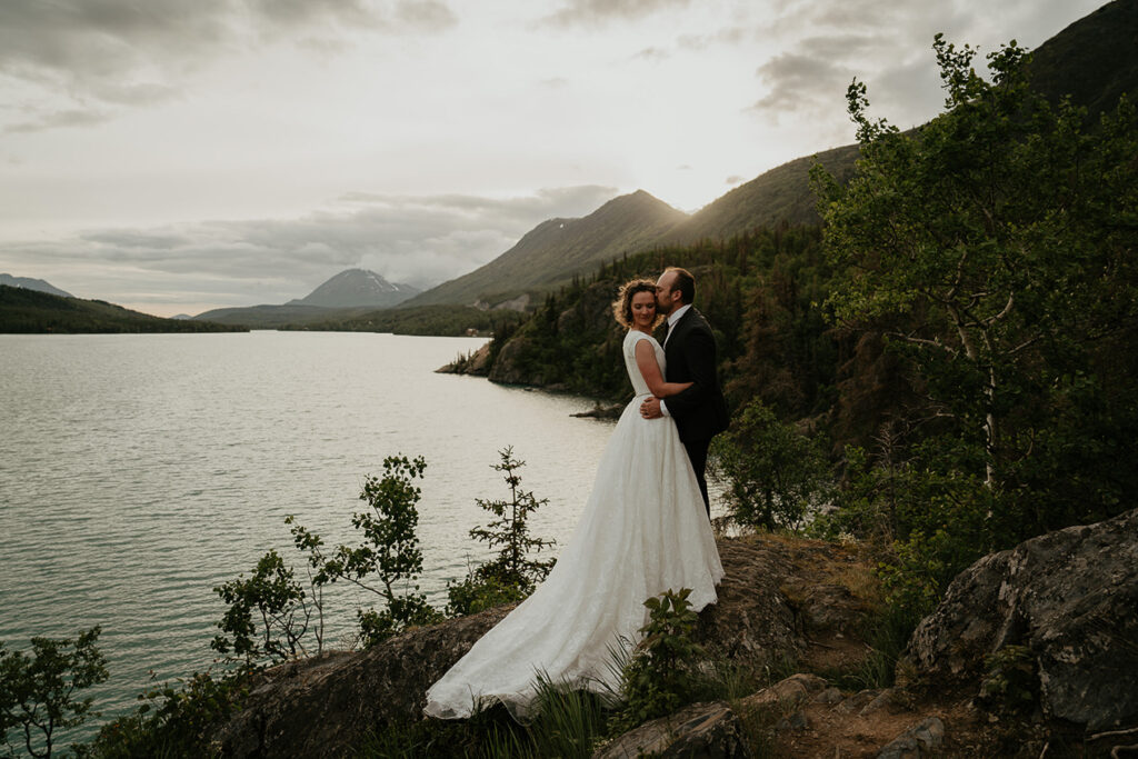 A couple kissing with mountains and the ocean in the background during their elopement in Alaska. 