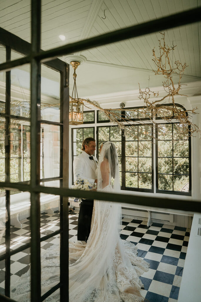 the bride and groom embracing each other in a sun room. 