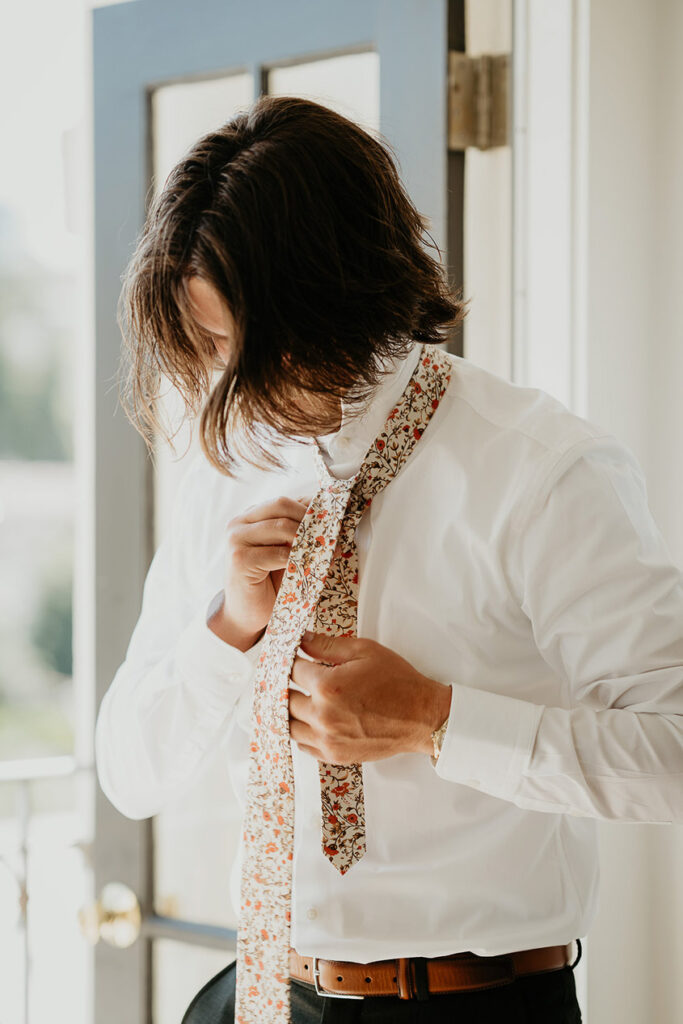 The groom putting on his tie. 